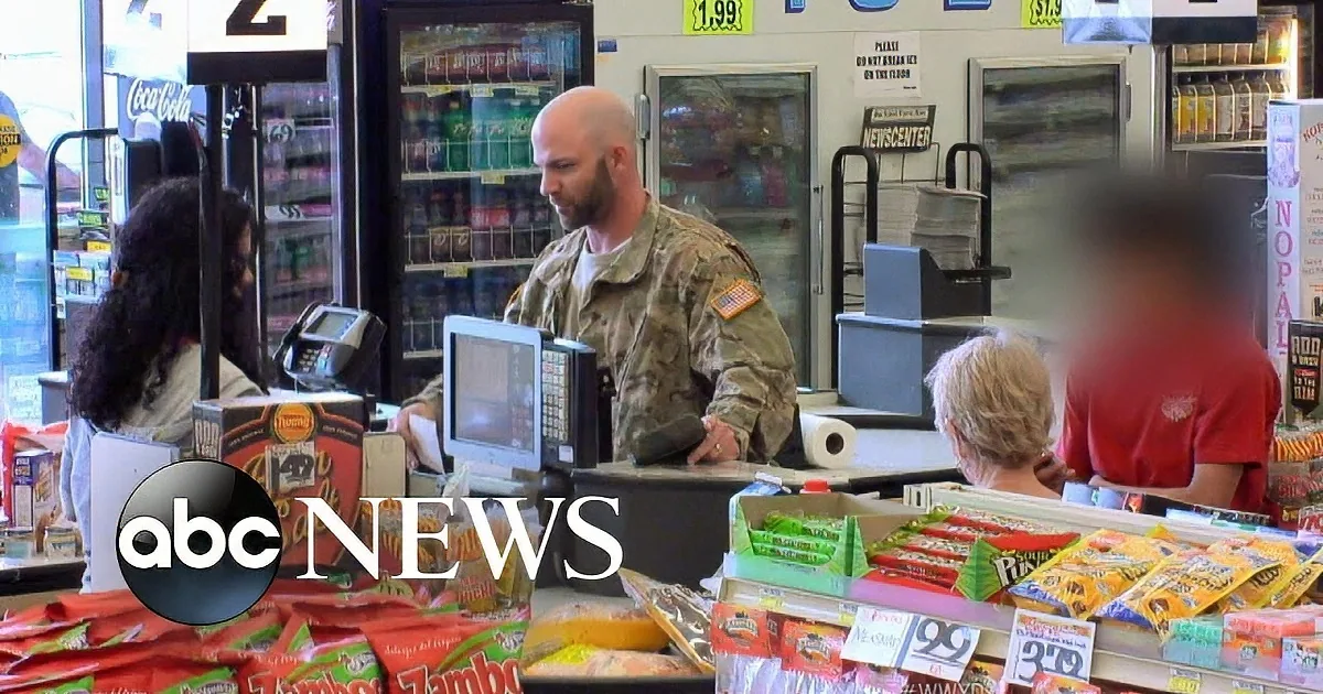 A soldier in uniform stands at a checkout counter in a grocery store, surrounded by customers and shelves of snacks.