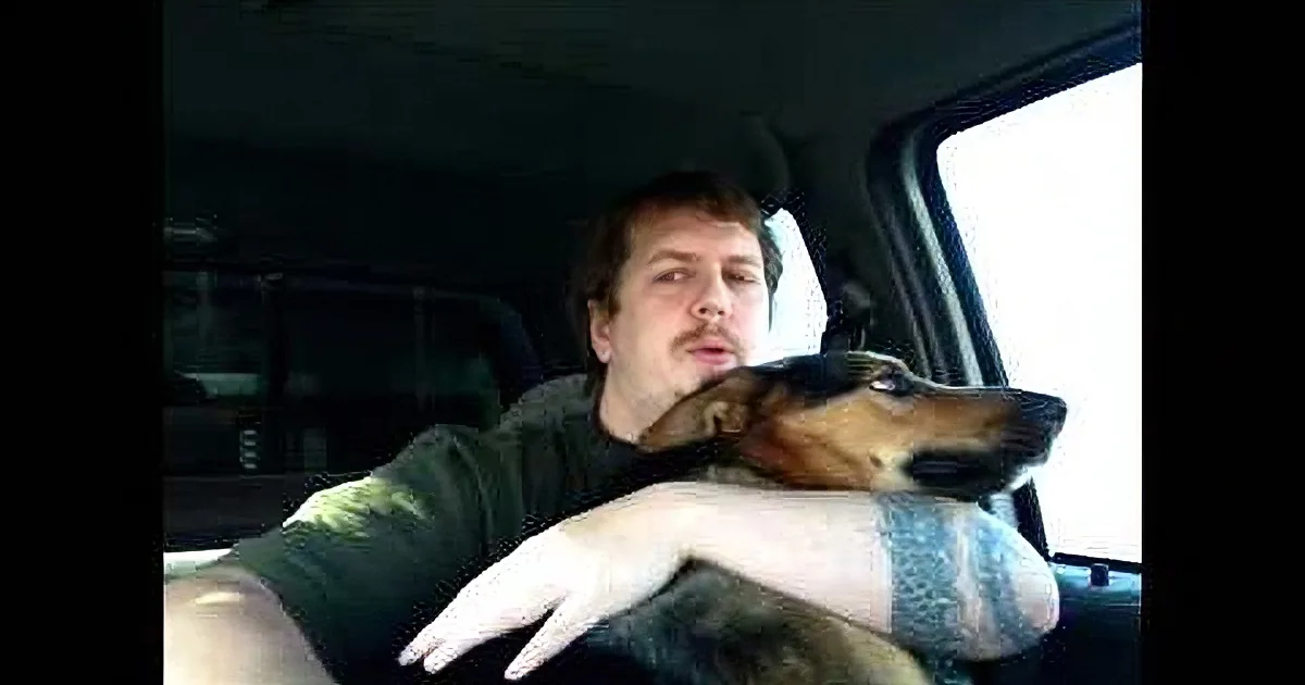 A man in a car with a dog resting its head on his arm, looking out the window.