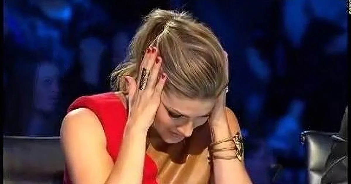 A woman in a red dress covers her face with her hands, appearing distressed.