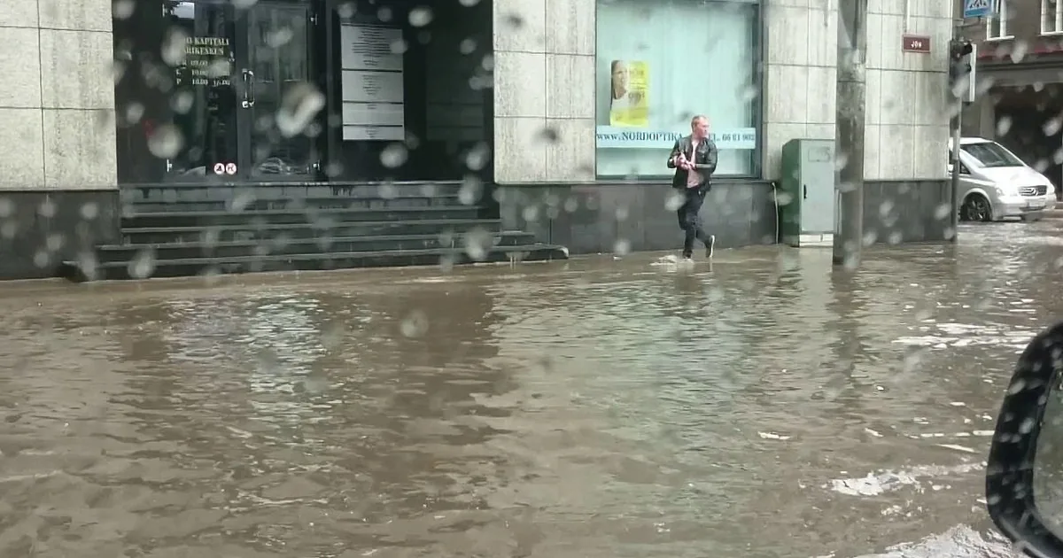 A man walks through a flooded street near a building with a sign.