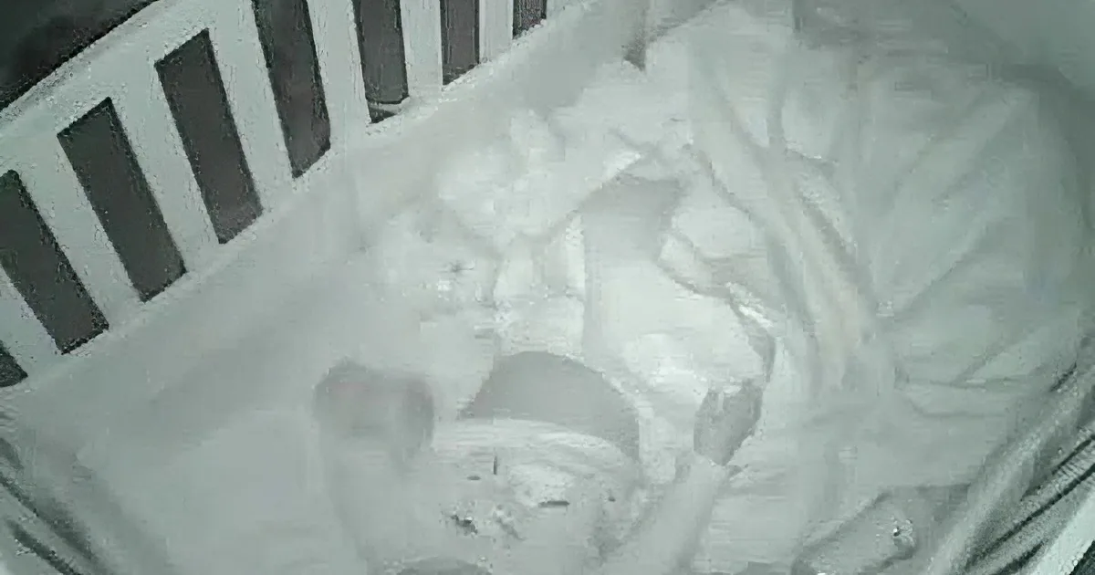 A baby in a white crib with a blanket and a white bow on its head.