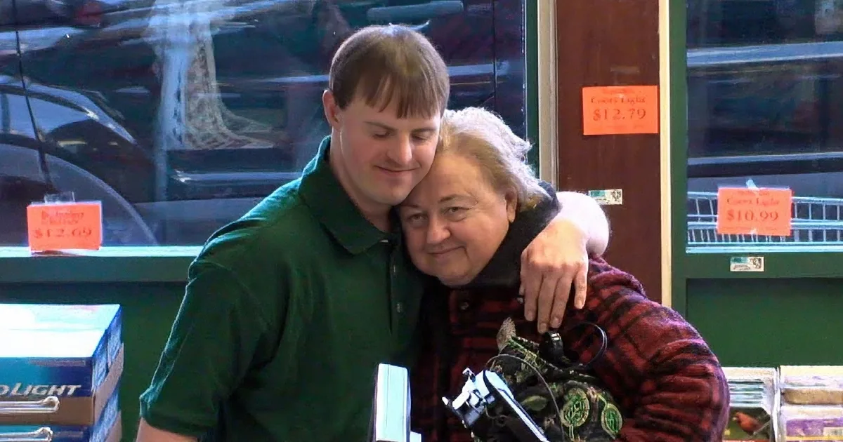 A smiling person in a green vest is reaching out to hand something at a checkout counter.