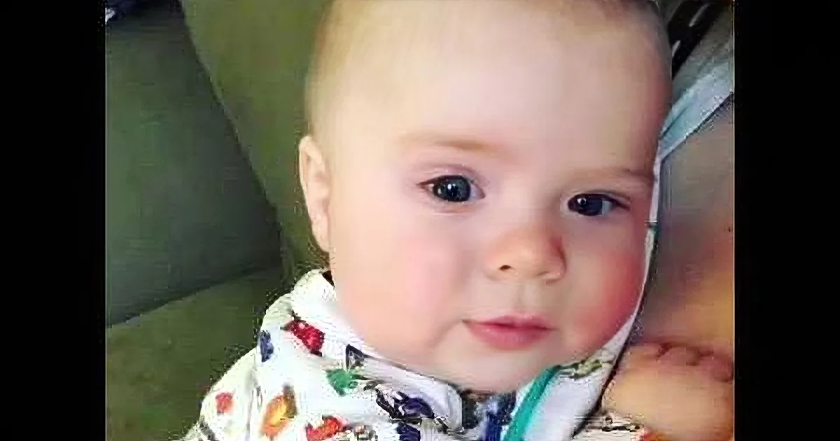 A baby with short hair and colorful pajamas looks directly at the camera.