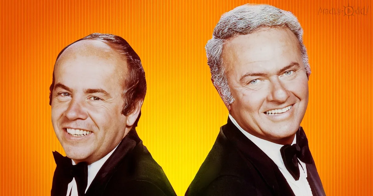 Two men in tuxedos smile against an orange background, one with a receding hairline, the other with gray hair.
