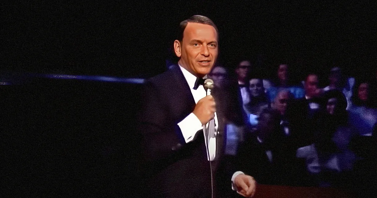 Frank Sinatra in a suit, holding a microphone, with a dark background and blurred audience.