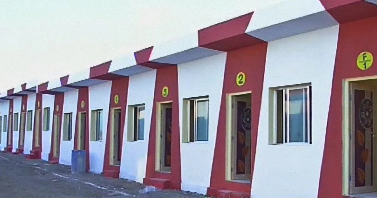 A row of identical red and white houses with numbered doors stands in a line.
