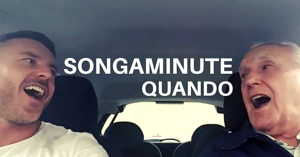 Two men in a car, one pointing and both looking upwards, possibly reacting to something outside the frame.