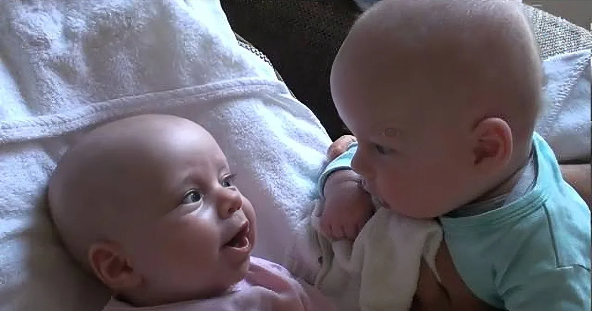 Two babies, one smiling and one looking down, lying on a white towel.