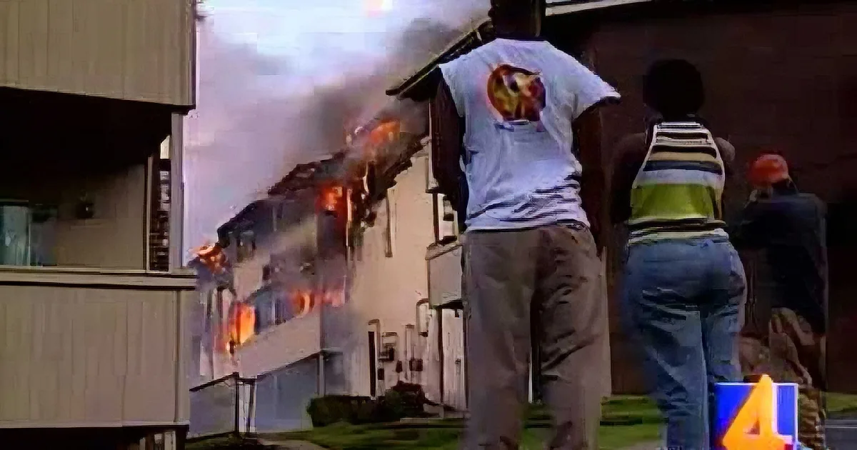People watch as a building on fire emits thick smoke and flames.