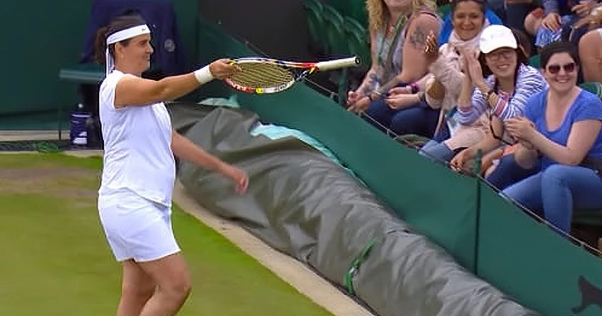 A tennis player swings her racket while spectators watch and clap on a grass court.