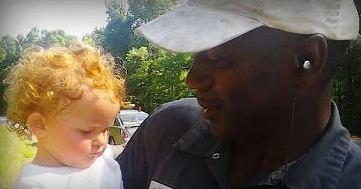 A man wearing a white cap and a dark shirt holds a young child with curly blonde hair.