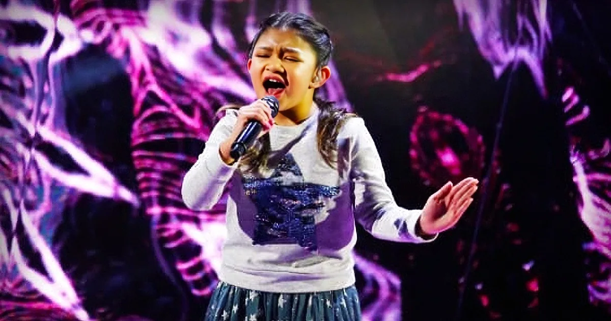 A young girl sings passionately on stage, wearing a white and black outfit with a skirt, against a vibrant, abstract...