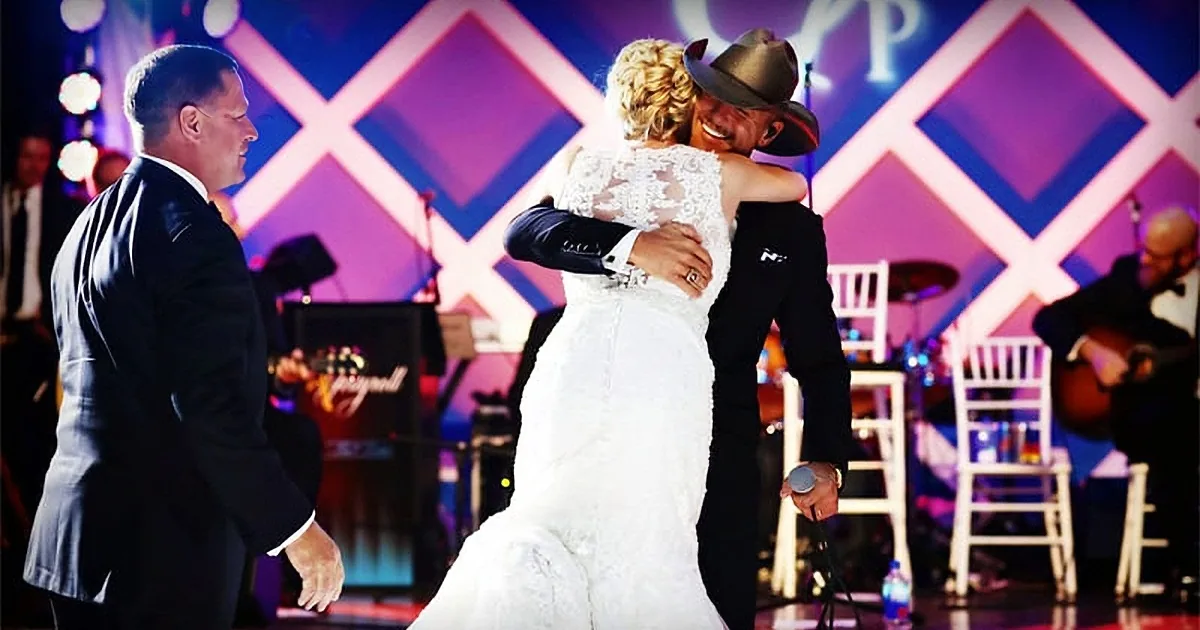 A bride in a white dress and groom in a suit share a joyful dance on stage.