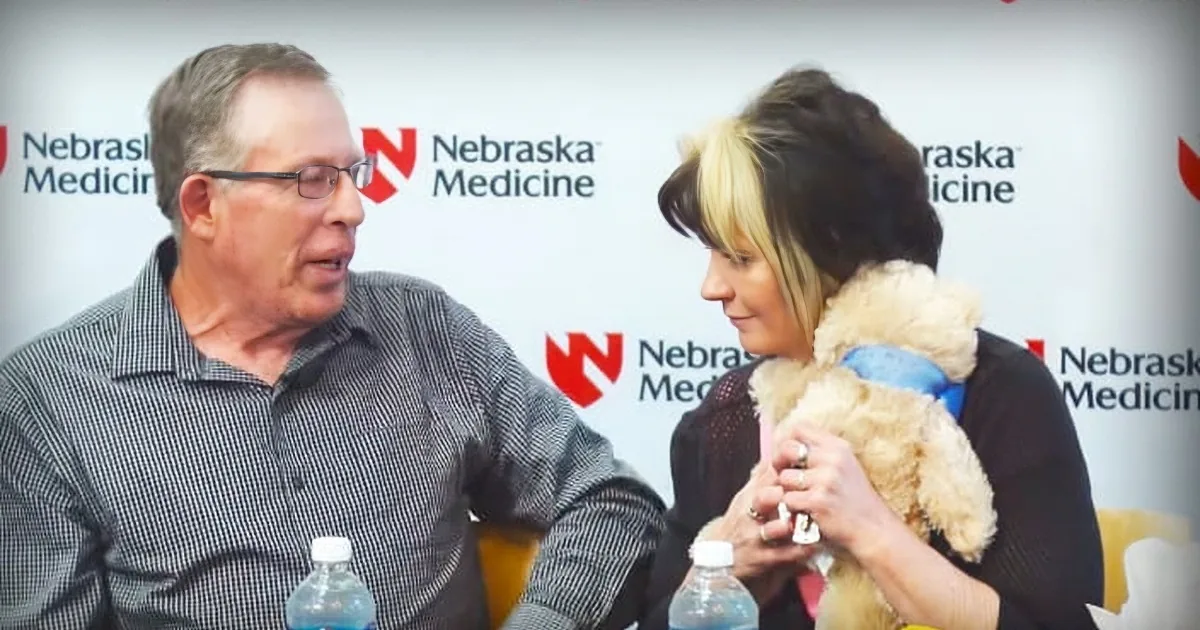 A man and woman are engaged in conversation, with the woman holding a teddy bear and a bottle of Aquafina water.