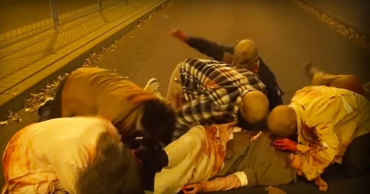 A group of people in yellow and plaid shirts are huddled together on a street, seemingly in distress or exhaustion.