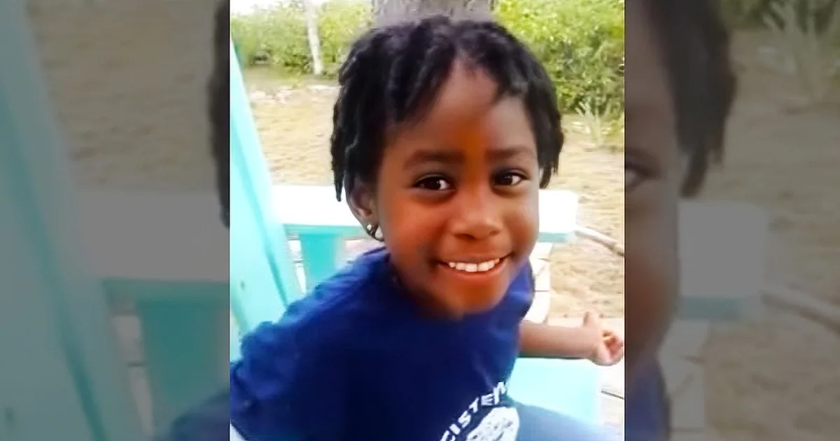 A young child with braided hair wearing a blue shirt smiles while holding a toothbrush.