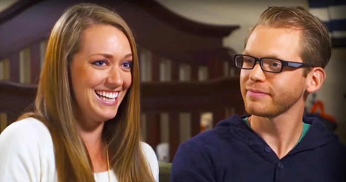 A smiling woman with long brown hair and a man wearing glasses and a dark shirt are seated together.