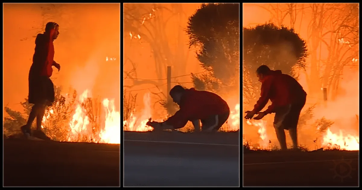 A person in a red jacket runs, bends, and picks up something amidst a fiery, orange-tinted environment.
