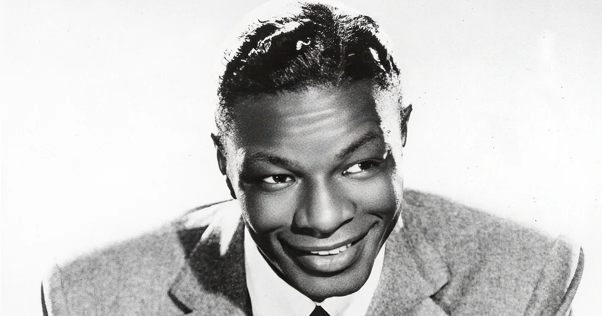 A smiling man with short hair, wearing a suit, against a plain background.