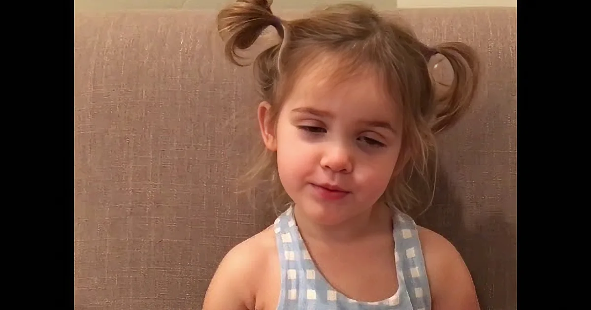 A young child with pigtails and a blue top looks directly at the camera.