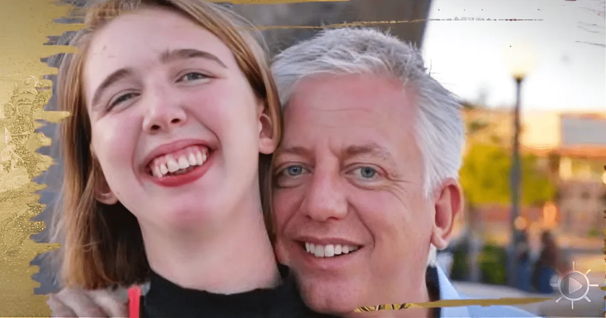 A smiling young woman and older man pose together in a lively outdoor setting.