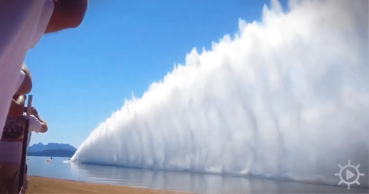 A massive wave of white smoke or fog rises dramatically from a body of water, creating a striking visual against a clear...