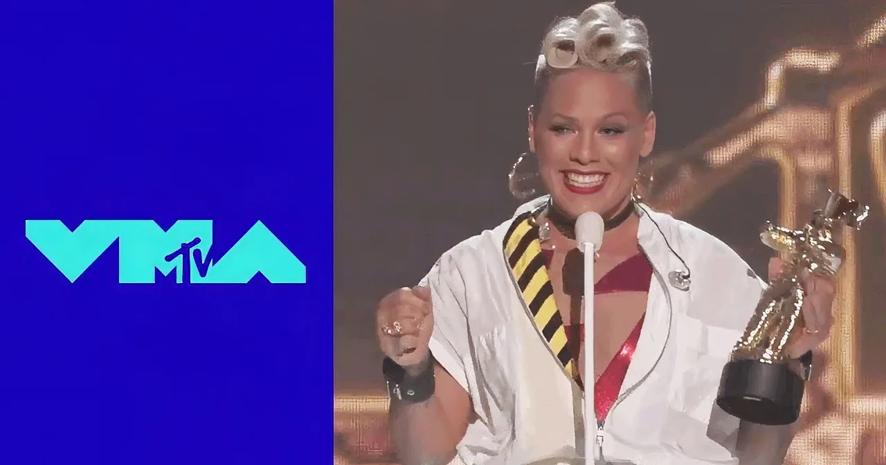 Pink holds an award at the MTV VMAs, smiling and wearing a white outfit with a yellow and black striped scarf.