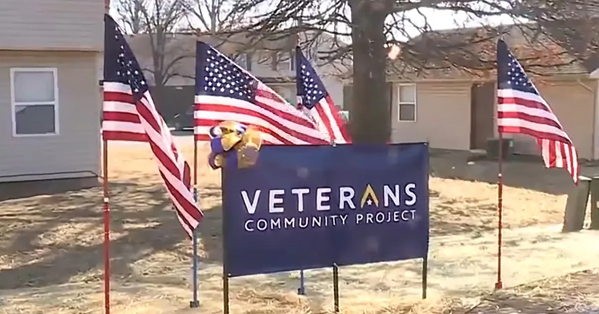 A sign for the Veterans Community Project is surrounded by American flags in a residential area.