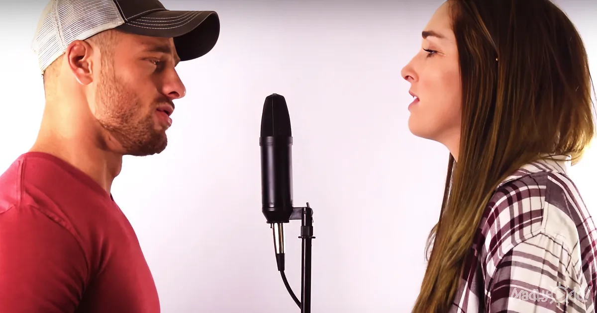 A man and woman sing into a microphone in a recording studio.
