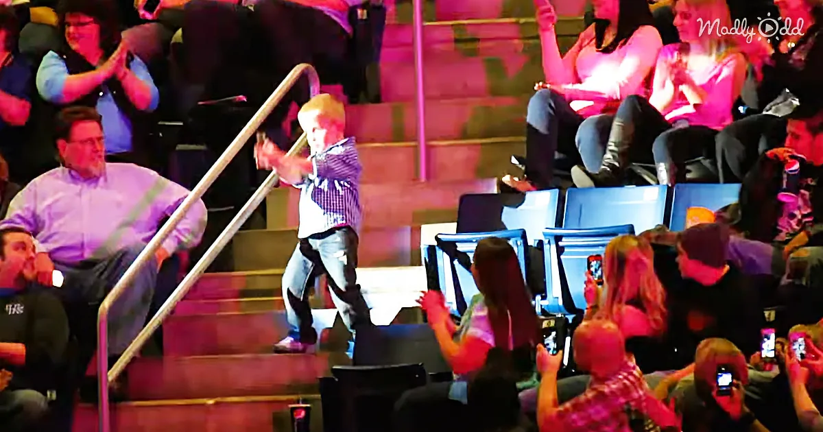 A young boy in a plaid shirt and jeans is running up a set of stairs in front of an audience.