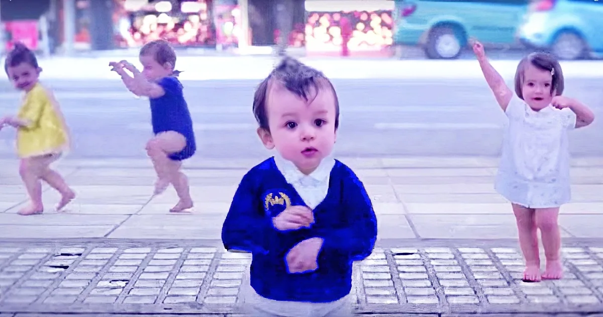 A baby in a blue sweater stands in the foreground, surrounded by other children playing on a sidewalk.