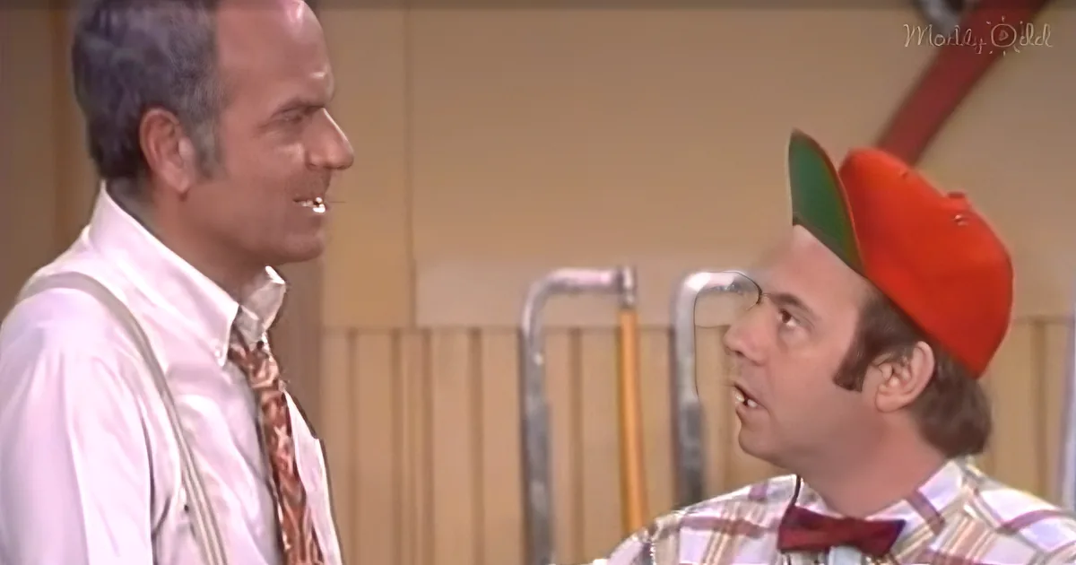 A man in a white shirt and tie is facing another man wearing a red hat and plaid shirt in a room with a ladder and wall.