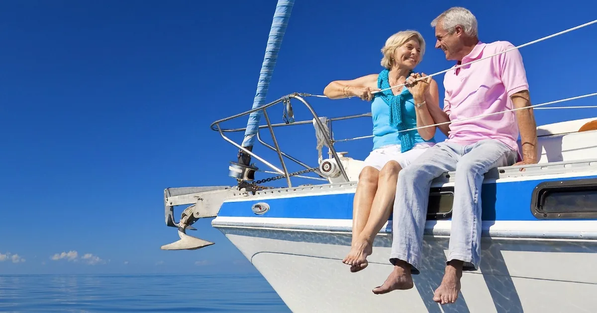 A couple sits on a sailboat's bow, enjoying a sunny day on the water.