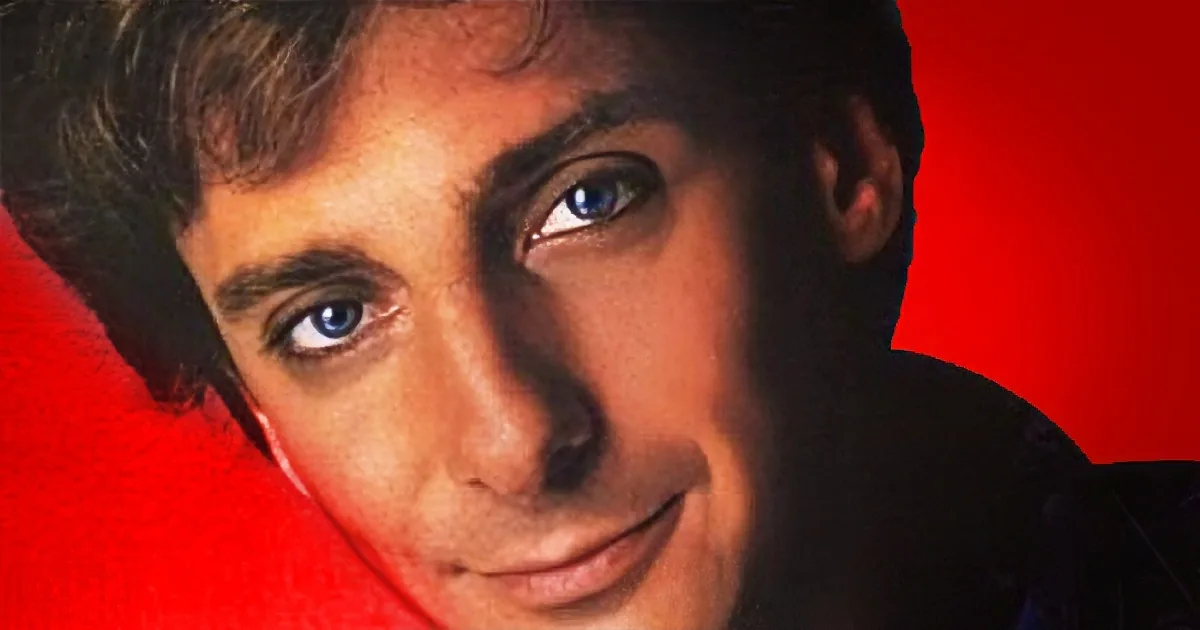 A close-up of a person with short, dark hair and blue eyes against a red background.