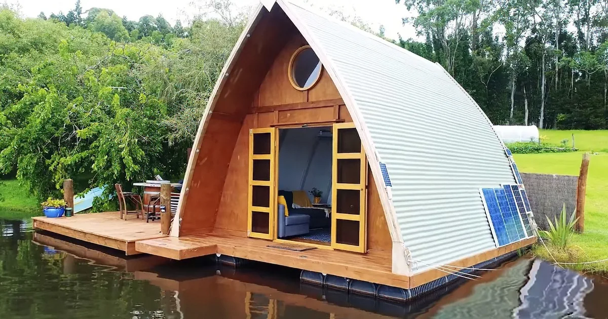 A modern, eco-friendly A-frame cabin floats on water, featuring solar panels and a cozy interior.