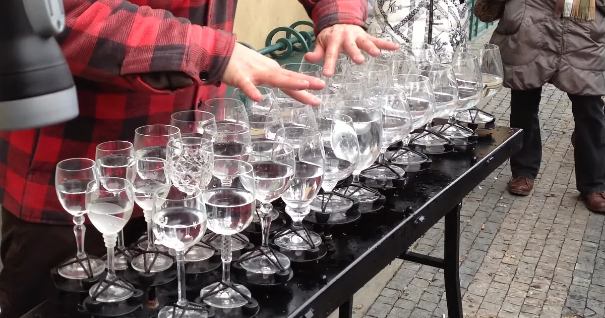 A person in a red plaid shirt arranges wine glasses on a table outdoors.