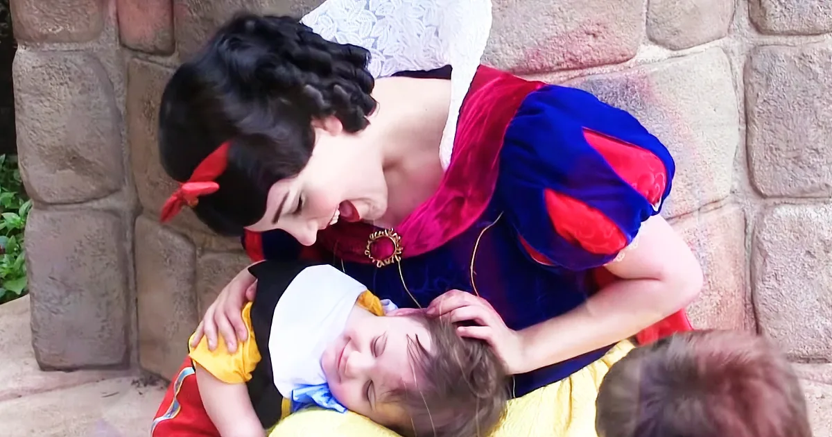 A person dressed as Snow White leans over another person in a similar costume, both smiling.