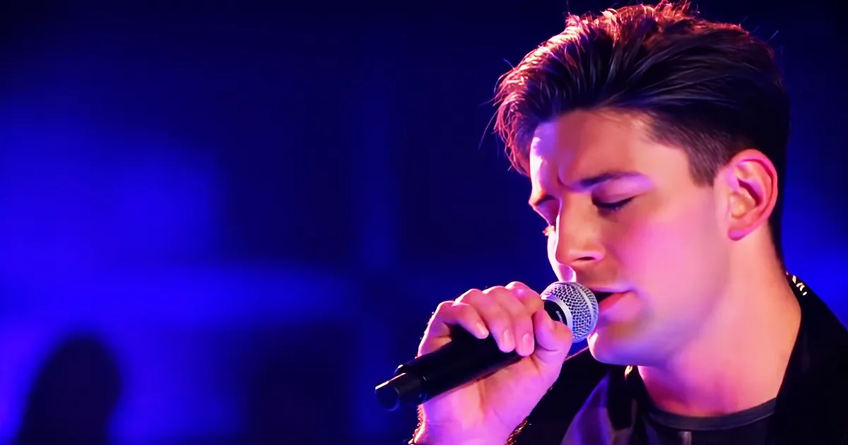 A person singing into a microphone under blue stage lighting.