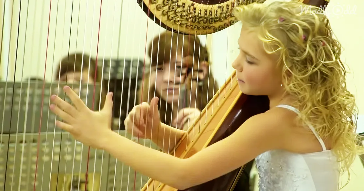 A young girl with curly blonde hair plays a harp, her fingers on the strings.