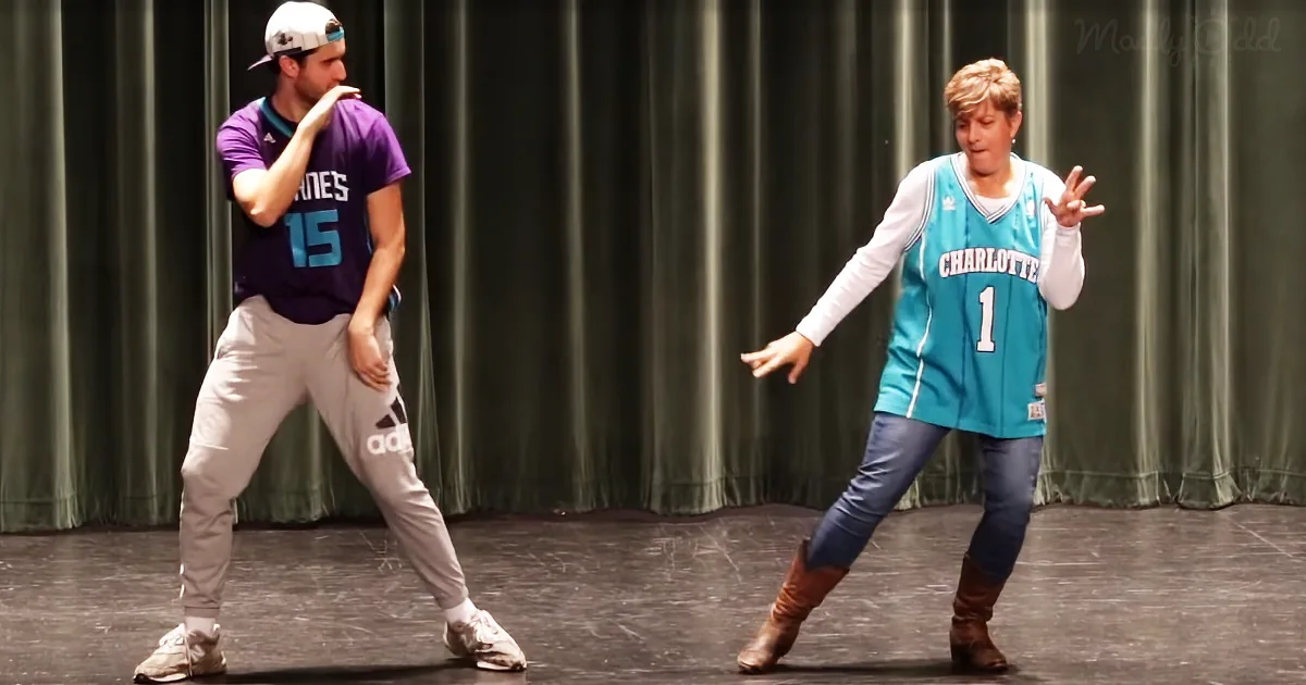A man in a purple jersey and a woman in a teal basketball jersey are dancing on a stage.