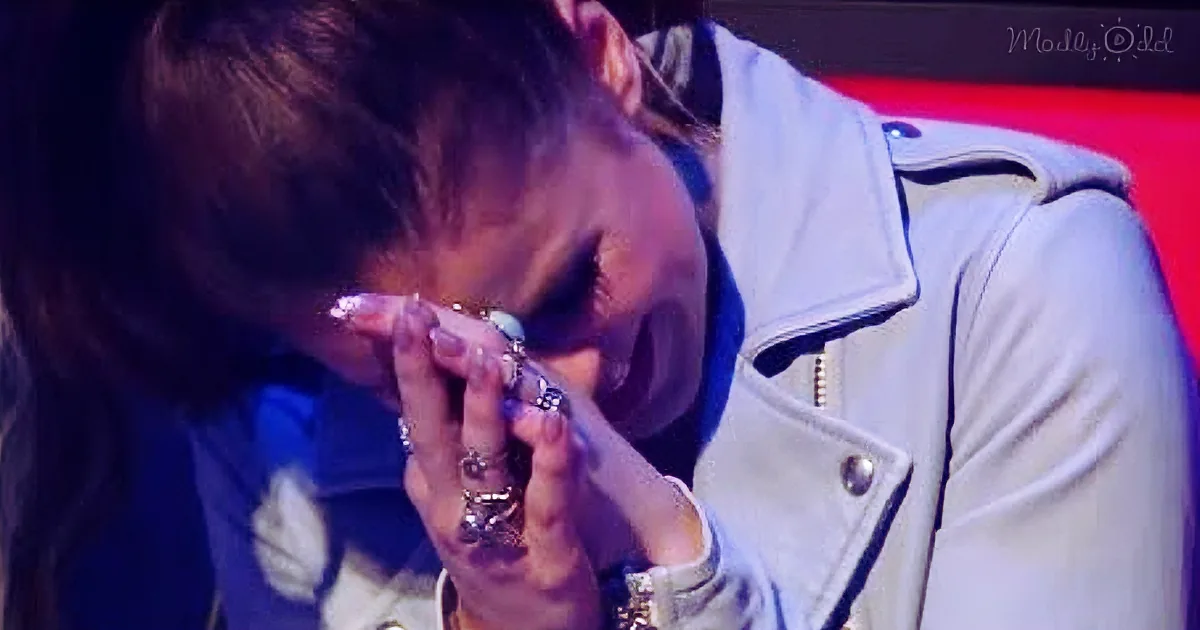 A person in a white jacket covers their face with hands adorned with multiple rings.