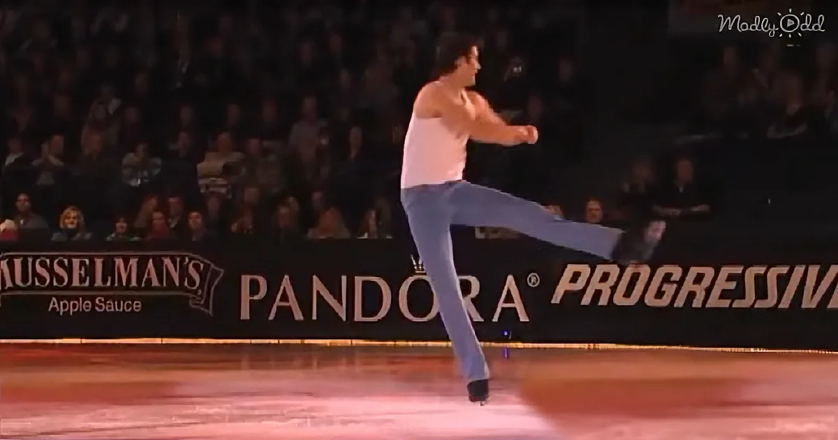 A man in a white tank top and jeans skates on ice, performing a kick with one leg extended.