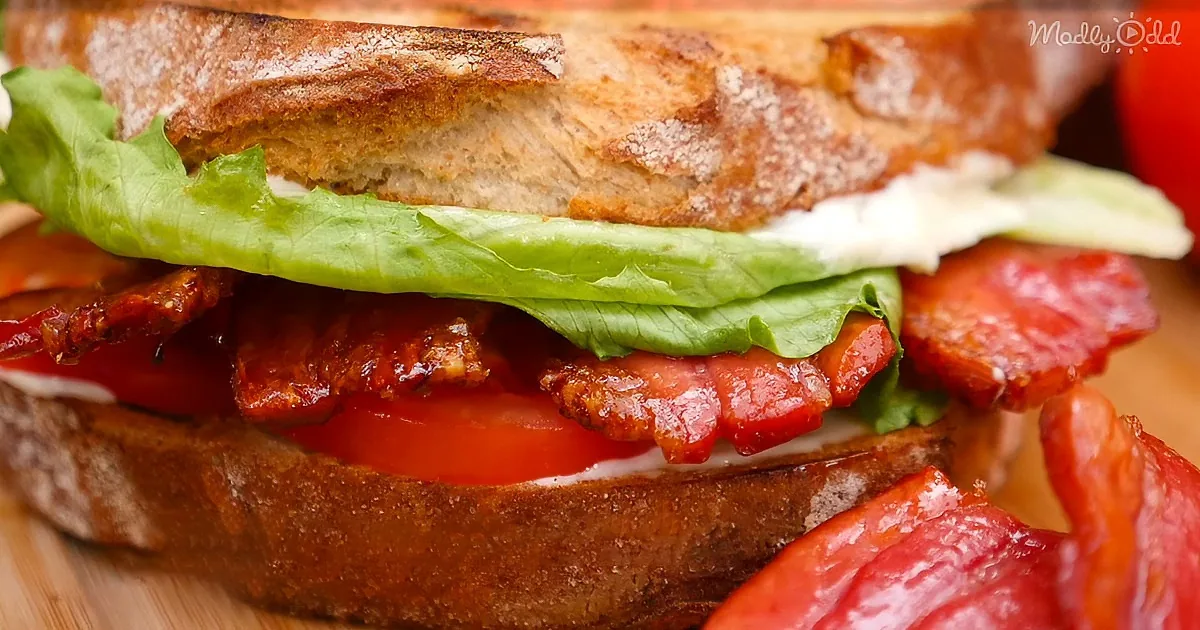 A close-up of a BLT sandwich with crispy bacon, fresh tomato, lettuce, and creamy dressing on toasted bread.