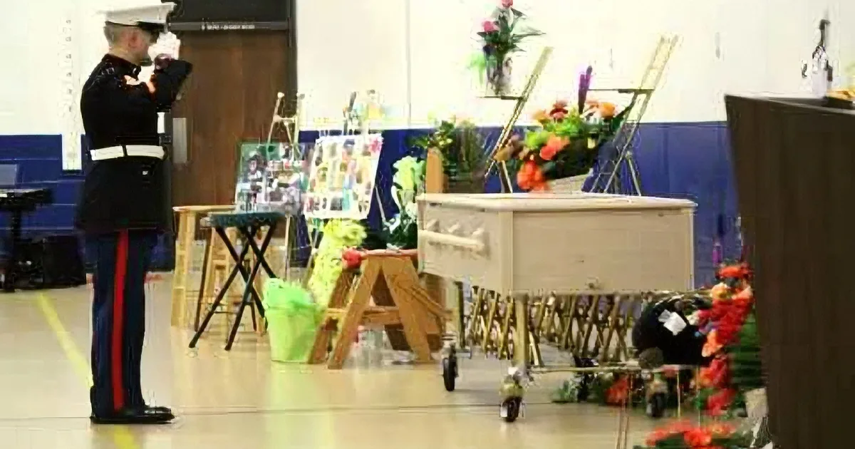 A Marine salutes solemnly at a memorial service with a casket adorned with flowers and personal items.