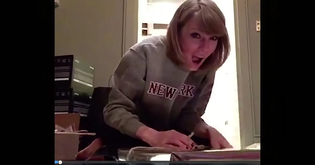 A person in a "NEW YORK" sweatshirt is sitting at a table, appearing surprised or excited.