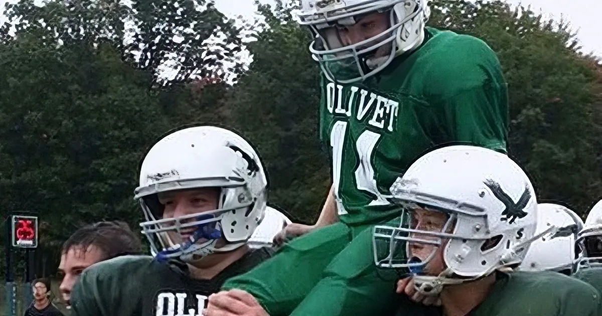 A football player in a green uniform with "OLIVET" and the number 11 is being carried by teammates in white helmets.