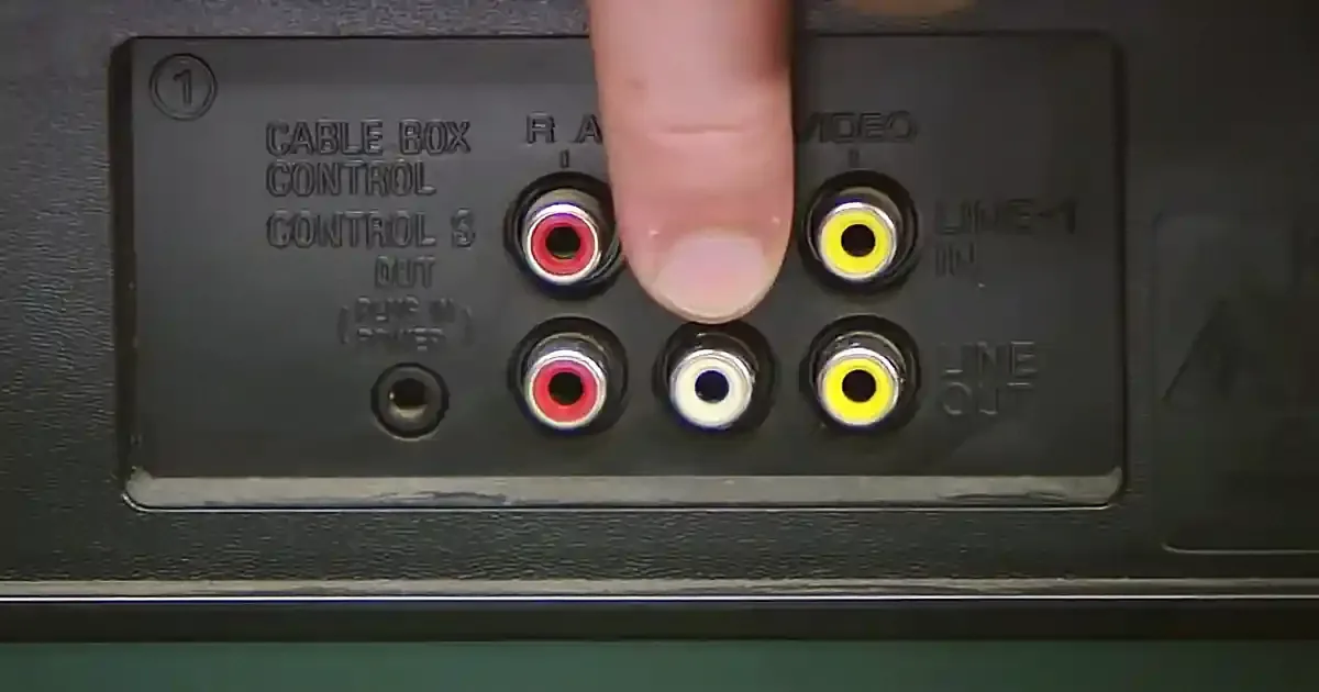 A finger points at a yellow RCA connector on a device's back panel.