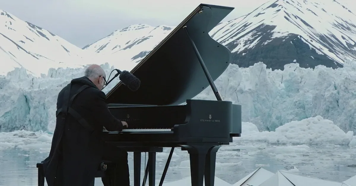 A man plays a Steinway grand piano in front of a snowy mountain backdrop.