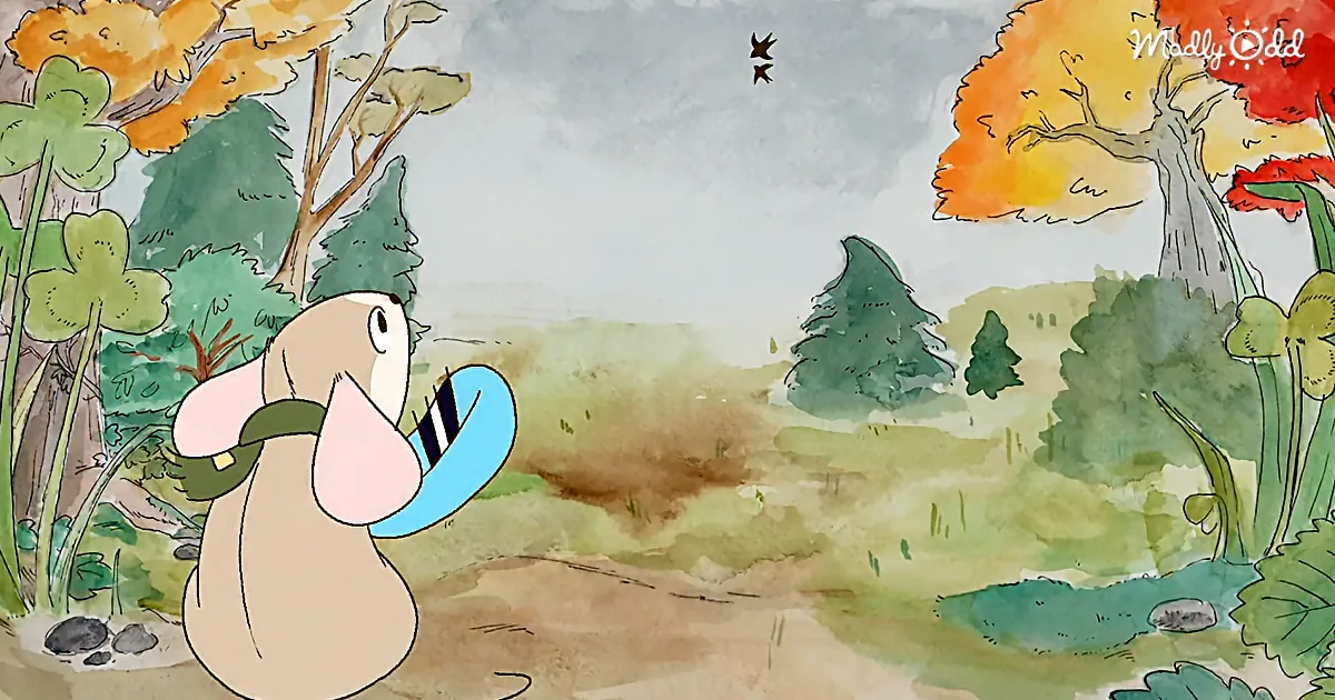 A beige dog with a blue collar stands in a colorful, autumnal forest, looking up at two birds flying in the sky.