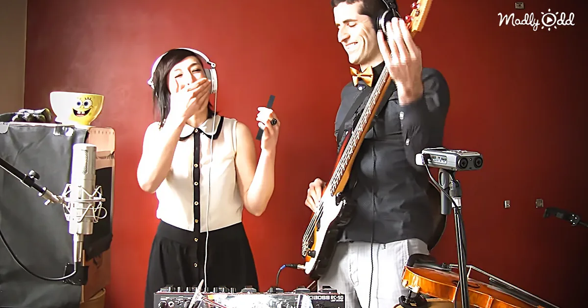 A woman in a white blouse and black skirt laughs while holding a microphone, next to a man playing a bass guitar.